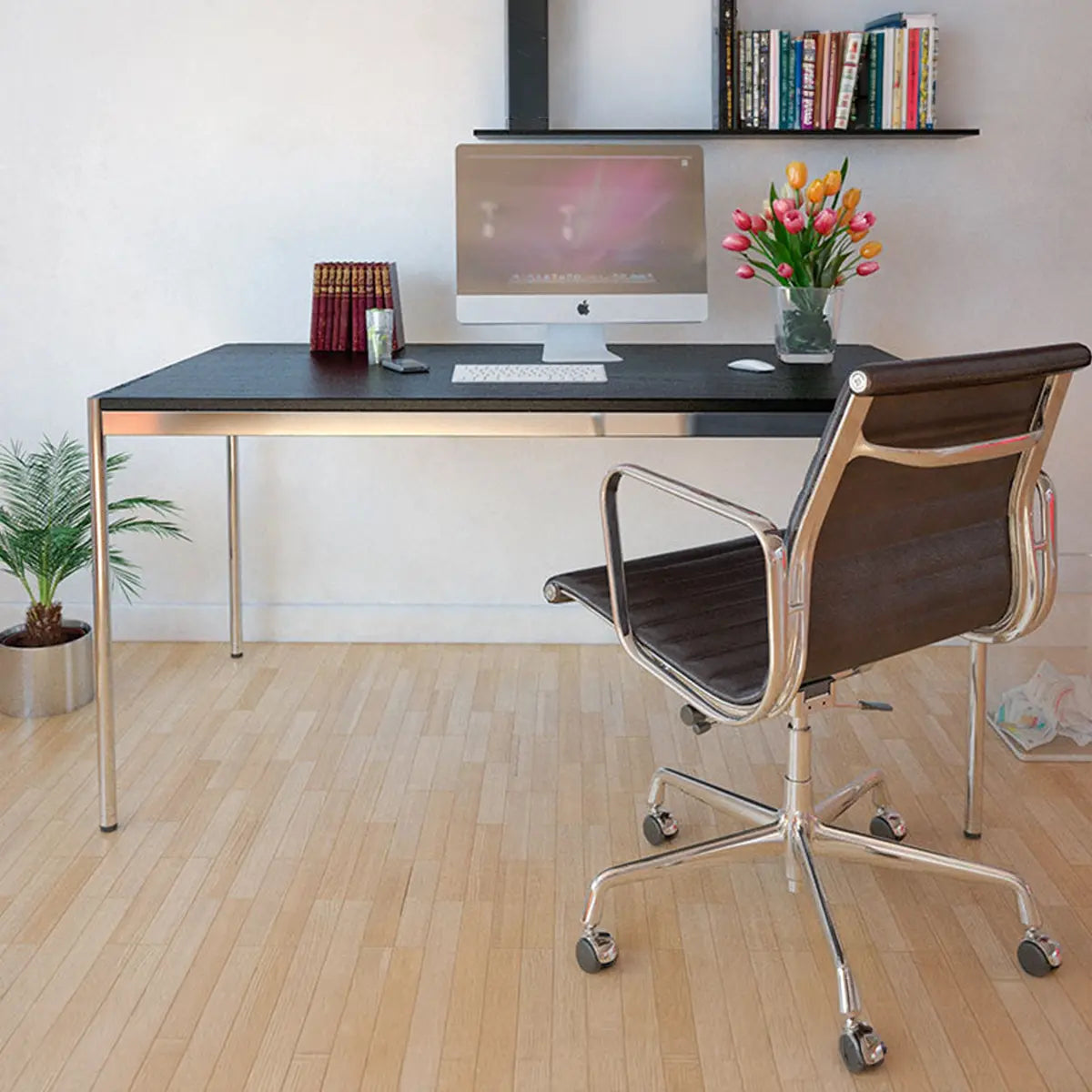 USM Haller Tisch in Schwarz als Arbeitsplatz mit Monitor, Blumenstrauss und Drehstuhl in hellem Raum