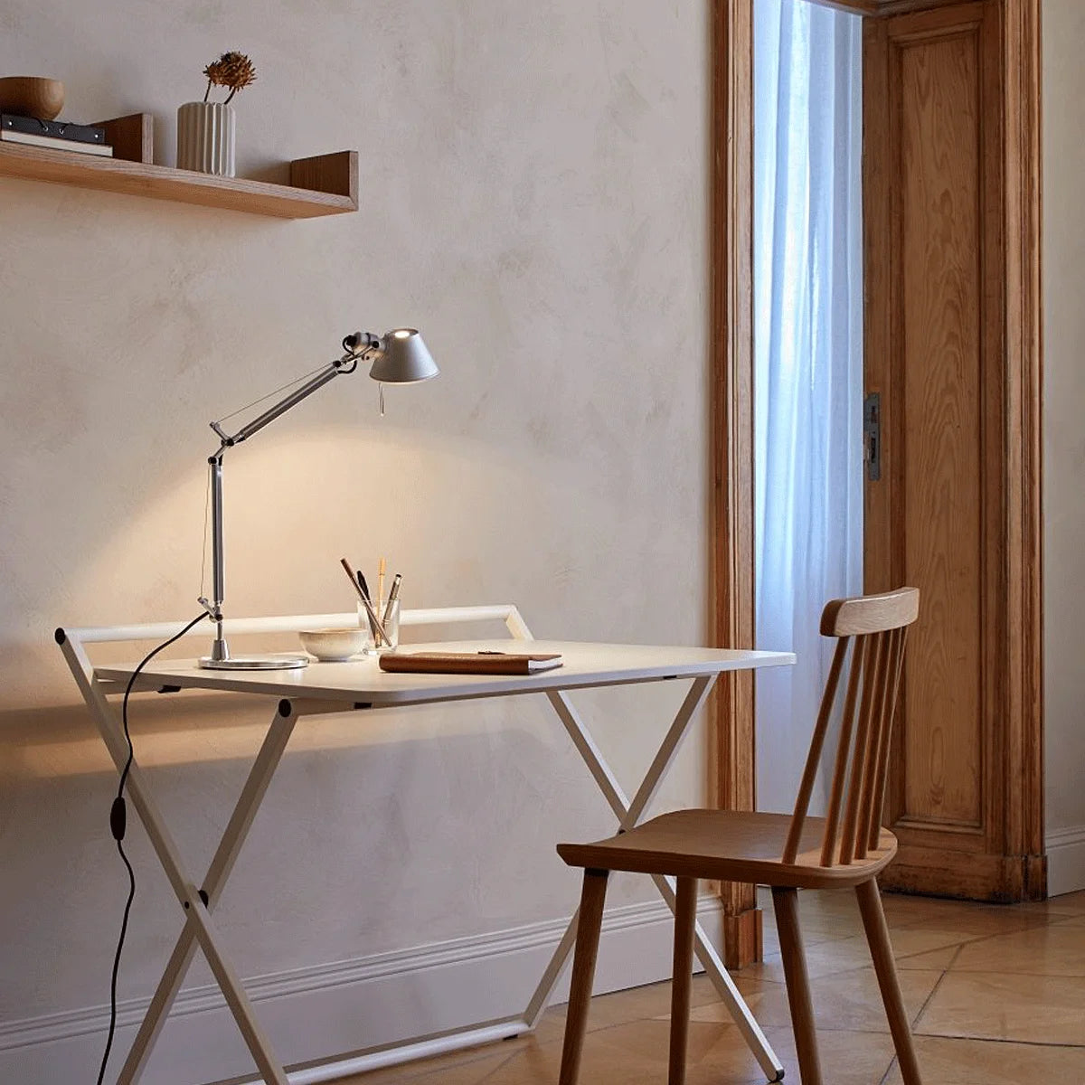 Artemide Tolomeo Tavolo Micro in Aluminium auf Schreibtisch, eingeschaltet, warmes Licht im Wohnambiente.