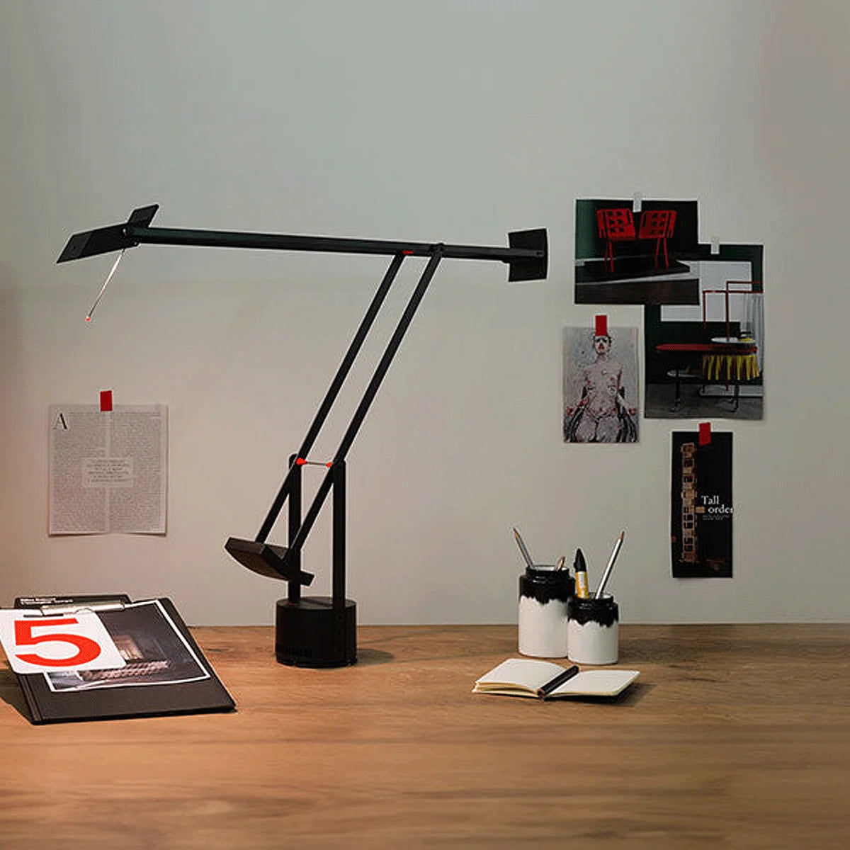 Artemide Tizio Tischleuchte in Schwarz, seitliche Ansicht auf Tisch, eingeschaltet mit sichtbarem Lichtkegel.