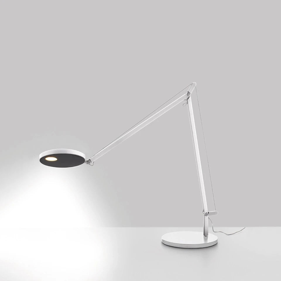 Eingeschaltene Artemide Demetra auf einem weißen Tisch vor grauen Hintergrund.