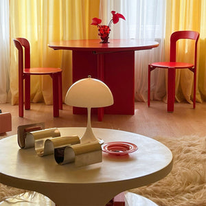 Wohnzimmer mit gelben Vorhängen, roten Designertisch und Stühlen und rundem Tisch mit Panthella 250 Tischleuchte mit Kabel.